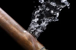 Water gushing from a broken copper pipe against a dark background, illustrating water damage issues relevant to repair services.